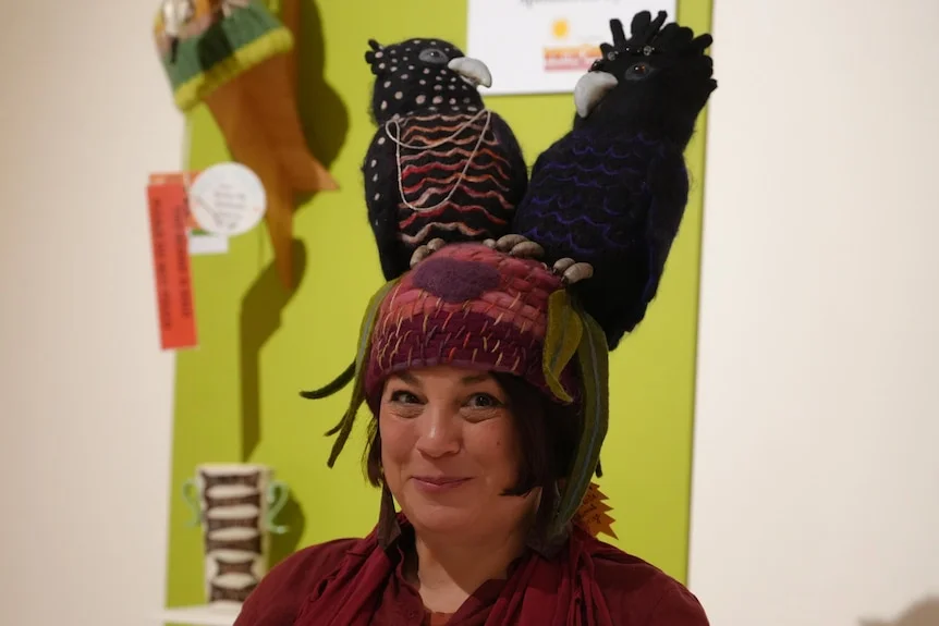 Maggie with short brown bob and red shirt, wearing a pink beanie which features two large black cockatoos on top of it.