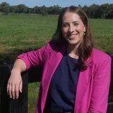 Amelia Bernasconi, wearing a bright pink jacket, leaning on a fence post.