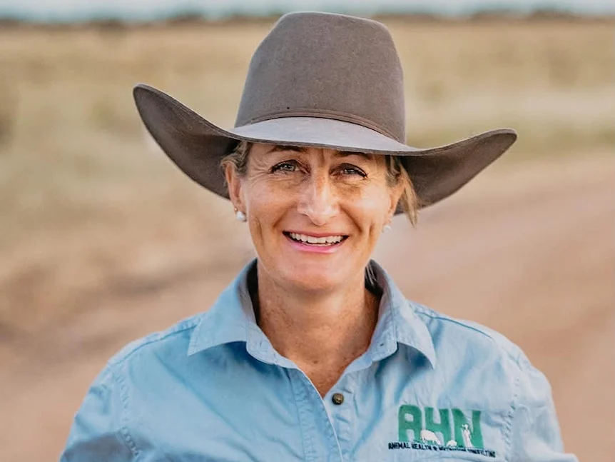 A woman in a brown felt hat smiles to camera