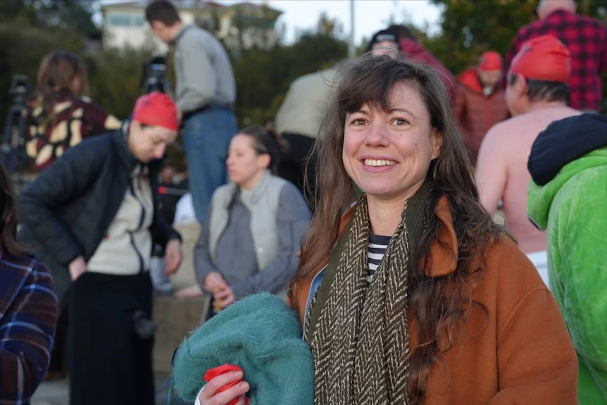 Jessica Nuel, a woman with brown hair and wearing a coat and scarf, smiles at the camera.