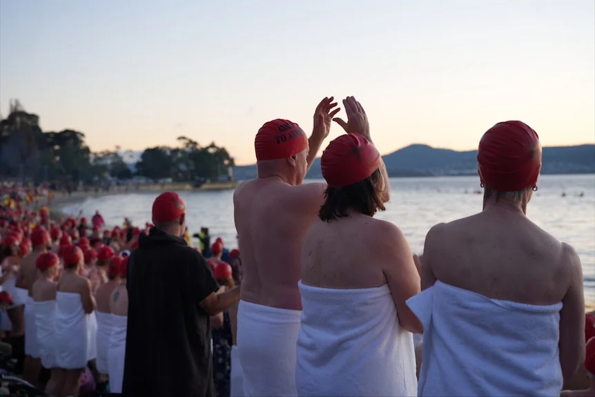 Groups of swimmers wearing towels prepare to enter the water for Dark Mofo's 2026 Nude Solstice Swim