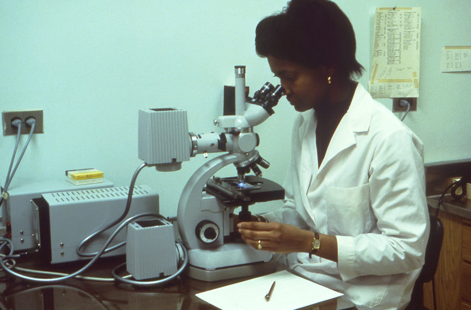 Woman in white lab coat looks through microscope