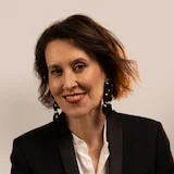 Virginia Trioli in a stylish suit on a set with lighting behind her