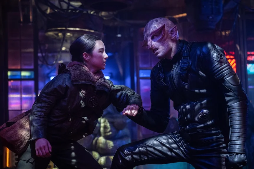 A young women stares down an alien in a bar