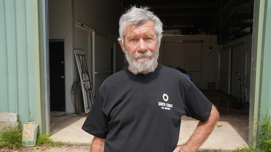 a man with a scruffy beard looks at a camera with a hand on his hip.
