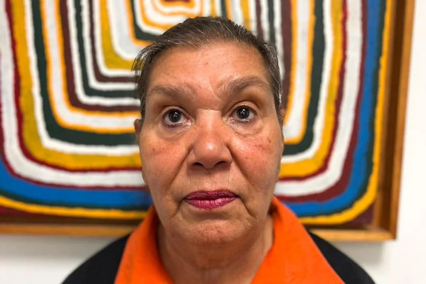 a woman wearing a orange shirt looks sternly at the camera 