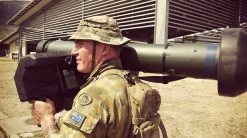 A man in army uniform with a launcher on his shoulder.