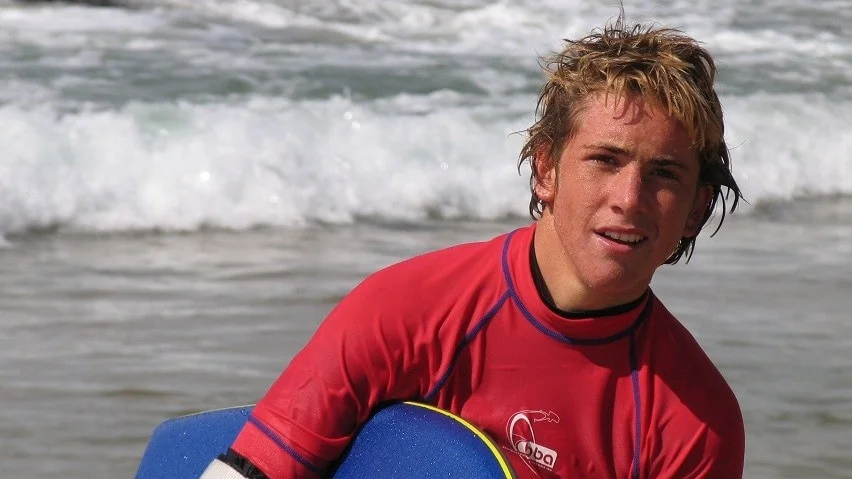 A young man holding a surboard at a beach