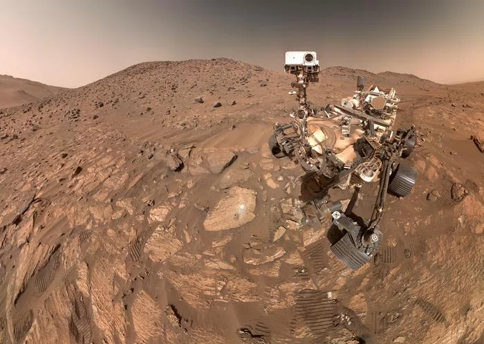 NASA's Perseverance Mars rover is seen in a selfie in July 2024 with the arrowhead-shaped Mars rock nicknamed Cheyava Falls in the Bright Angel region of the planet’s Jezero Crater. The rover collected two mudstones there that have complex carbon