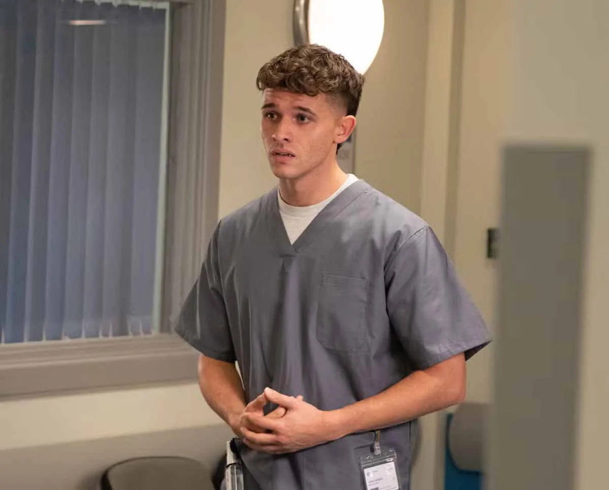 Jacob Gallagher standing in a hospital corridor, wearing scrubs, looking worried in Emmerdale.
