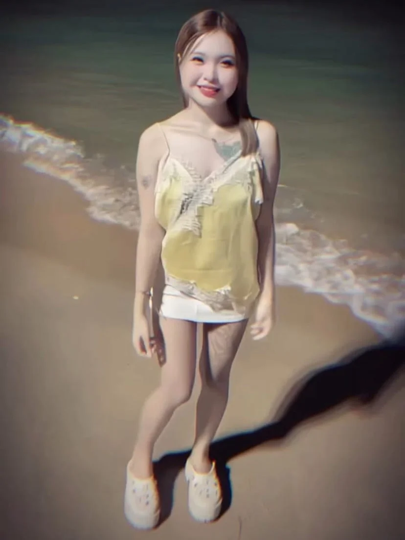 A 17-year-old Thai girl, smiling and standing on a beach.