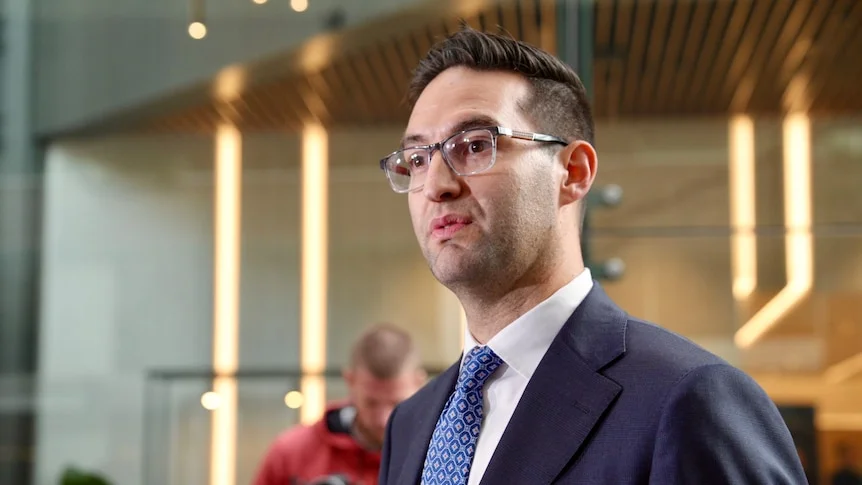 Joshua Burns in suit and blue tie wearing glasses outside royal commission