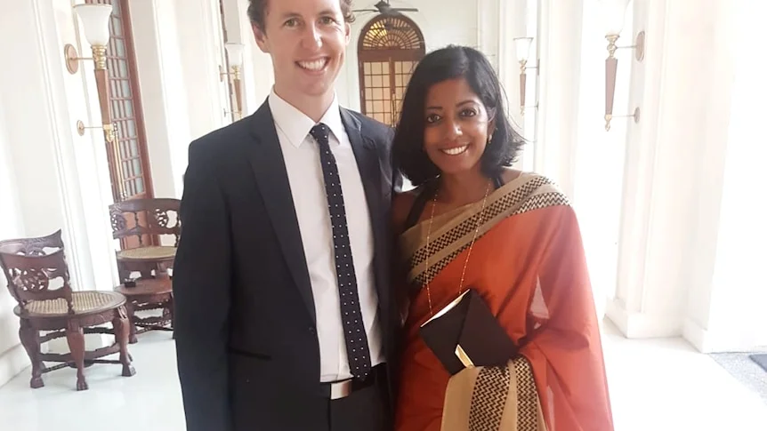 Sashi Perera stands next to her husband Charlie, wearing a burnt orange sari. Charlie wears a suit.