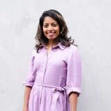 Portrait of writer and comedian Sashi Perera wearing a long shirt dress that is pale purple, with a green skirt.