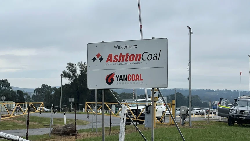 A sign reads welcome to Ashton Coal in front of gates with a car.